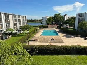 Community swimming pool featuring a paved deck, surrounded by manicured lawns and mature landscaping