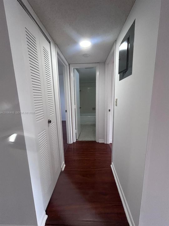 Hallway featuring wood-finish flooring, white louvered-door closet, and recessed ceiling lighting