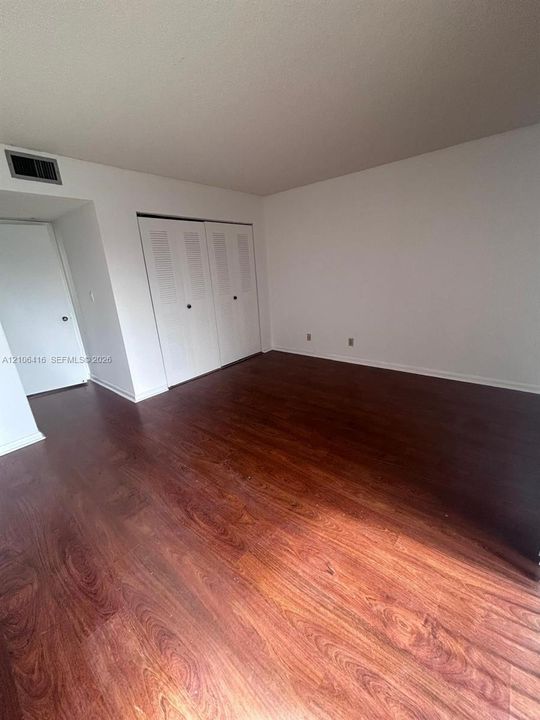Room featuring wood-finish flooring, white walls, and a dual-door closet with louvered panels