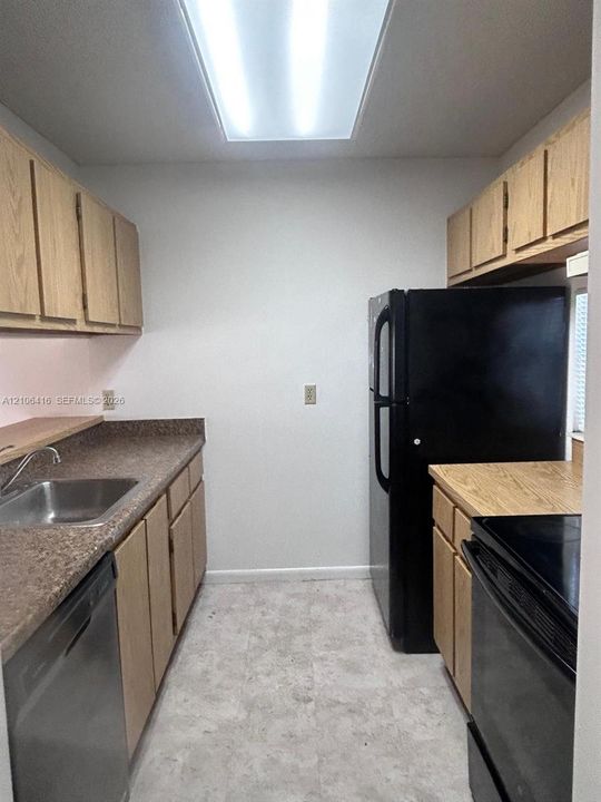 Kitchen featuring light-finish cabinetry, speckled laminate countertops, recessed fluorescent lighting, stainless steel sink, and black appliances
