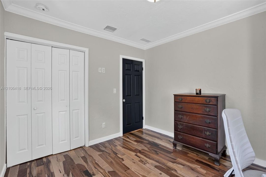 Room featuring wood-finish flooring, crown molding, a multi-panel closet door, and a contrasting six-panel interior door