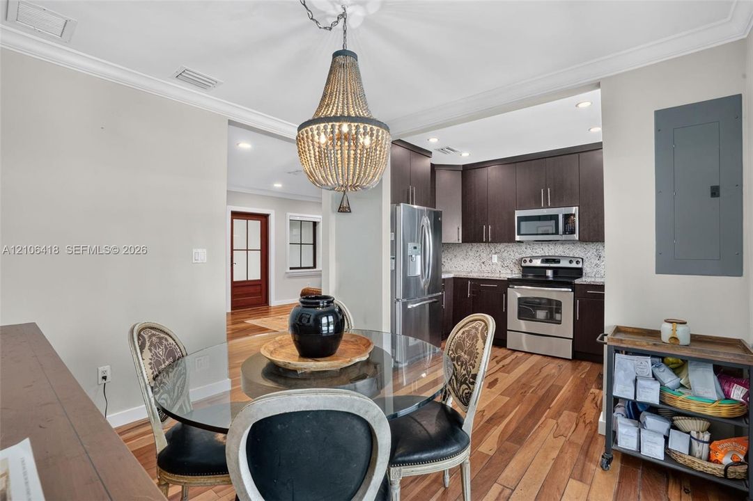 Kitchen featuring dark wood cabinetry, stainless steel appliances, and stone-finish backsplash, accented by a decorative beaded pendant light and wood-finish flooring