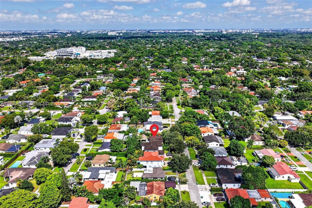 Aerial perspective of a multi-story residence featuring a terracotta-tiled roof, a spacious private backyard, and an integrated swimming pool, situated within a dense canopy of mature trees