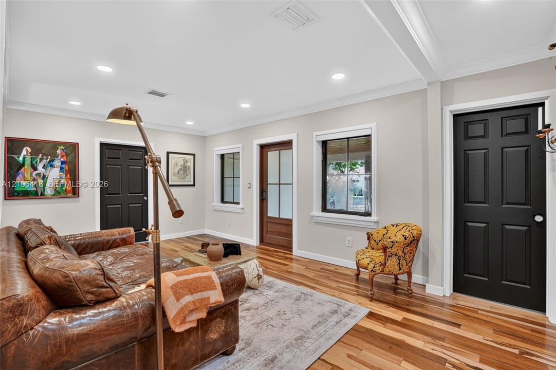 Living area featuring wood-finish flooring, recessed lighting, crown molding, multi-panel black interior doors, and a glass-paneled wooden exterior door