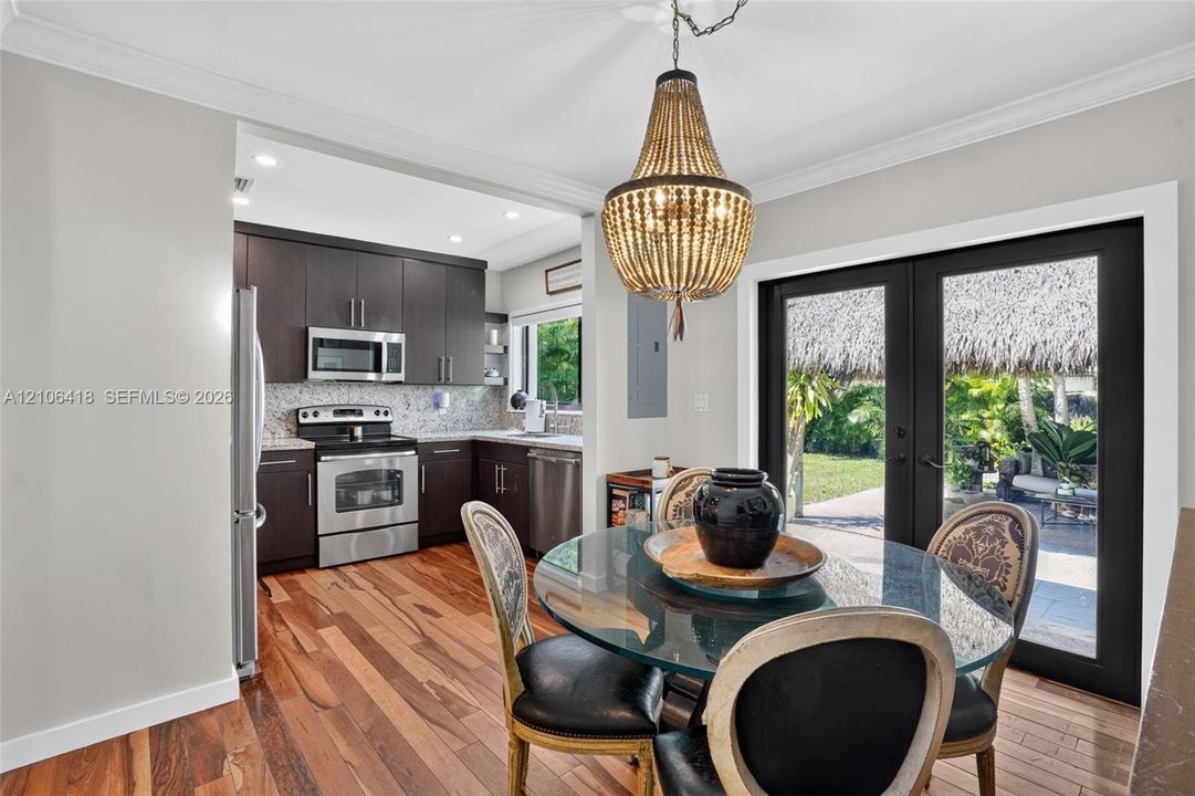 Kitchen featuring dark cabinetry, stainless steel appliances, wood-finish flooring, a tiered bead chandelier, and black-framed glass patio doors