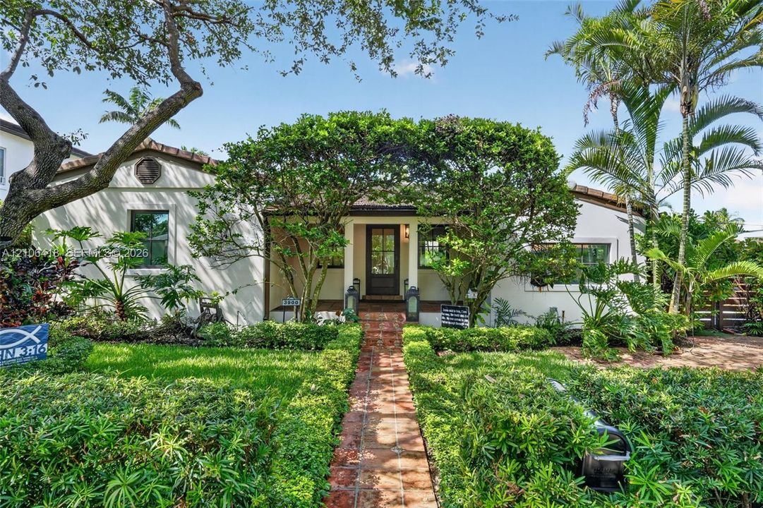 Stucco exterior residence featuring a clay tile roof, brick walkway, and landscaped garden beds
