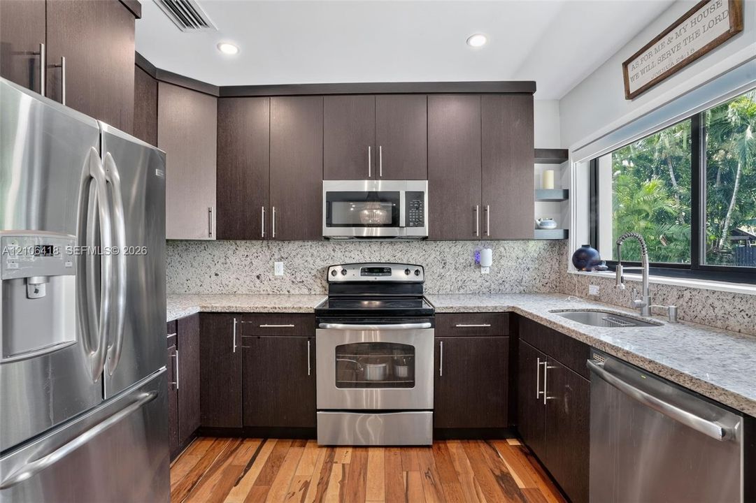 Kitchen featuring dark-finish cabinetry, stone-style countertops, stainless steel appliances, wood-finish flooring, and recessed lighting