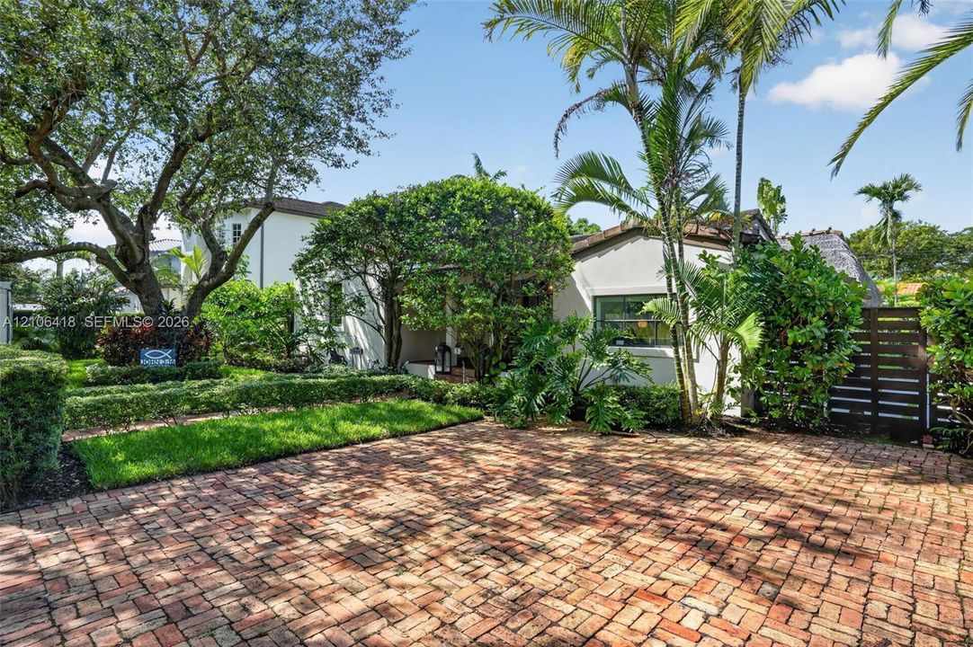 Stucco exterior featuring a brick-paved driveway, mature landscaping, and palm trees