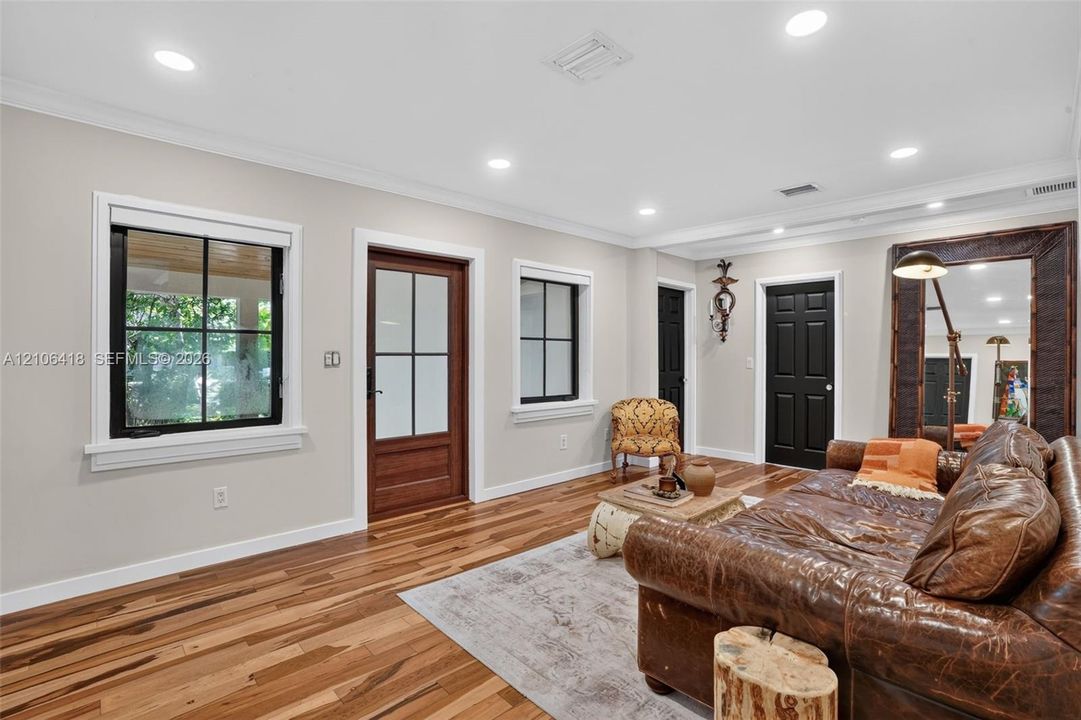 Living area featuring wood-finish flooring, recessed lighting, crown molding, multi-pane windows with black frames, and solid-core interior doors with black finish
