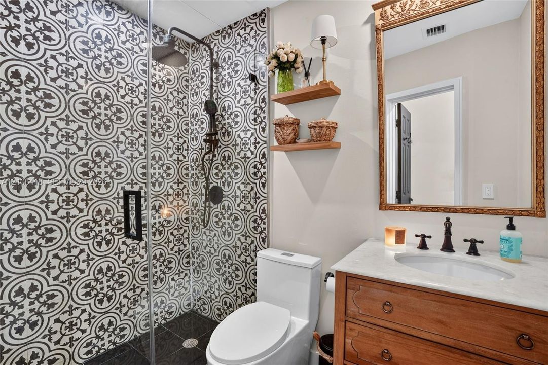 Walk-in shower featuring patterned tile surround, stone countertop vanity, wood-finish cabinetry, and wall-mounted shelving