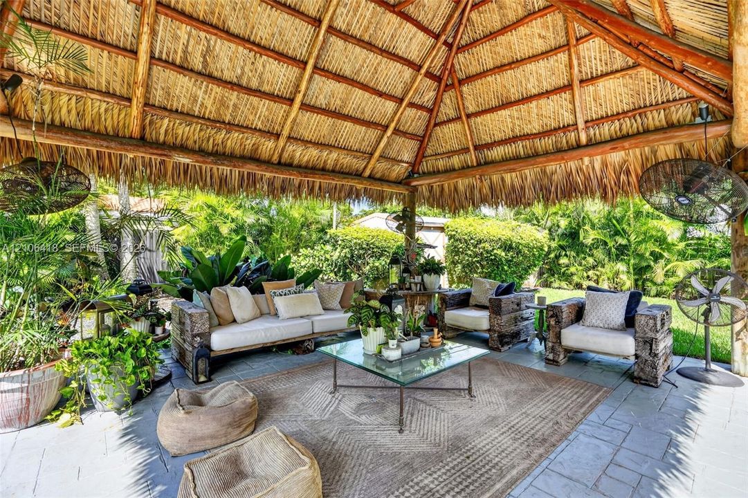 Open-air pavilion featuring a thatched roof, natural wood timber support beams, and stone paver flooring
