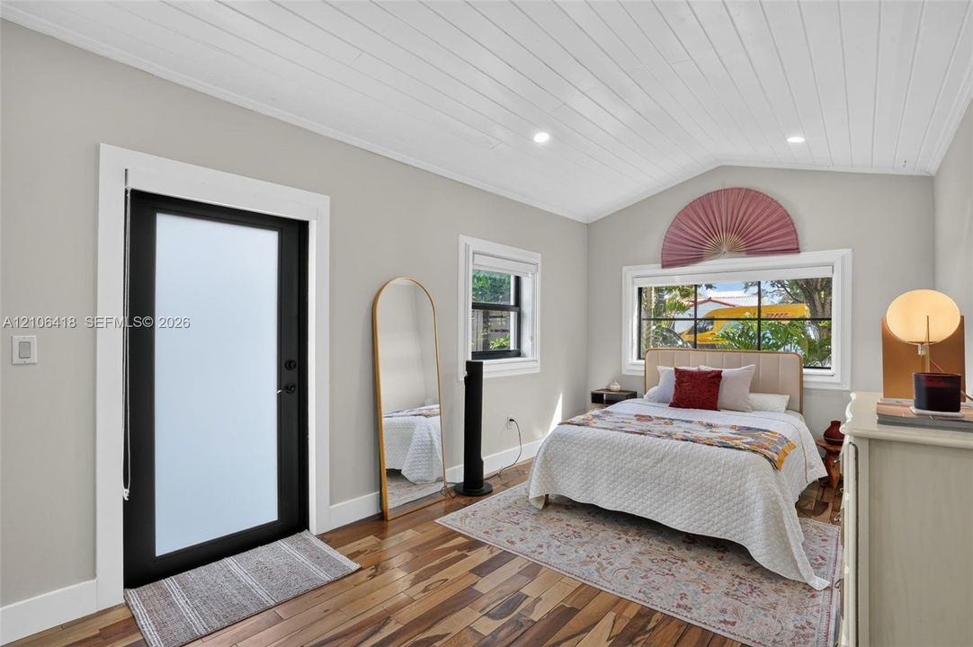 Vaulted ceiling with tongue-and-groove paneling, wide-plank wood-finish flooring, recessed lighting, and a black-framed door with frosted glass paneling
