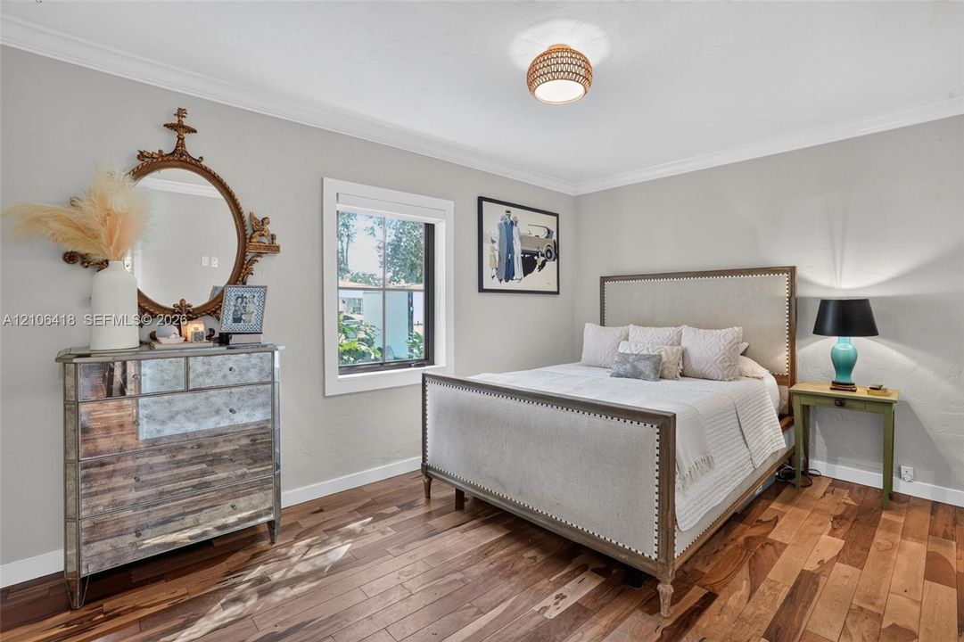 Neutral-toned interior featuring wood-finish flooring, crown molding, a single-pane window with white trim, and a textured drum-style flush-mount ceiling light fixture