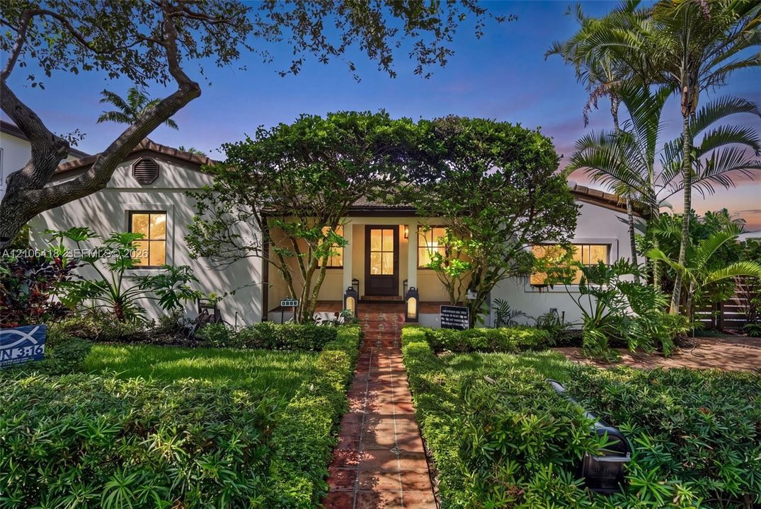 Stucco exterior featuring a tiled roof, covered entryway with a terracotta-tiled path, multi-pane windows, and manicured landscaping