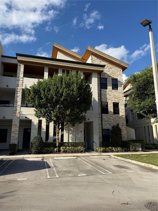 Multi-story exterior featuring stone veneer siding, split-pitch roofline, covered balconies, and paved parking area