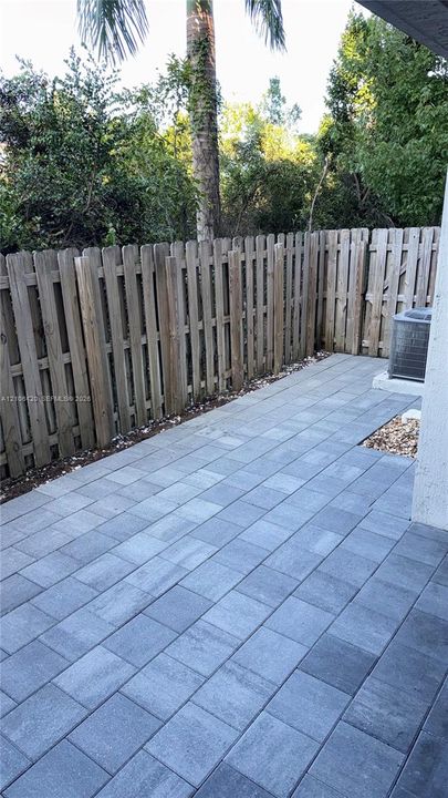 Private rear patio featuring grey stone pavers, vertical wood privacy fencing, and mature perimeter trees