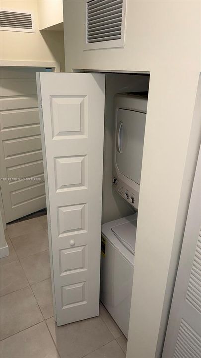 Stacked washer and dryer unit concealed behind a five-panel bifold door with ceramic tile flooring