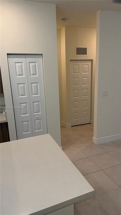 Neutral-toned ceramic tile flooring, solid-surface countertop, and two multi-panel closet doors