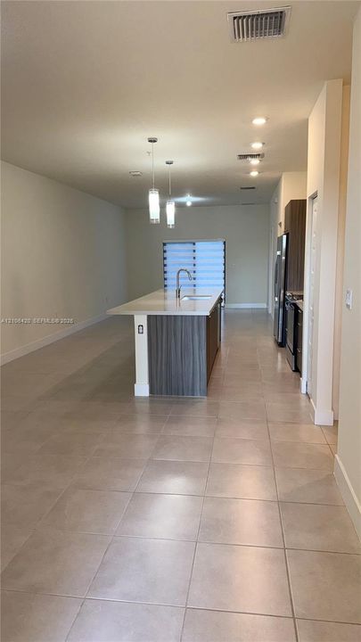 Kitchen featuring a central island with a stone-finish countertop and sink, two pendant lights, recessed ceiling lighting, wood-finish cabinetry, and neutral floor tiling