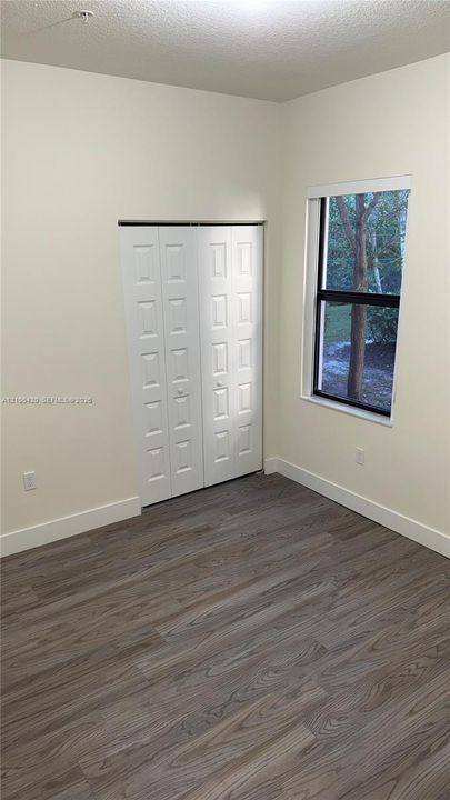Interior space featuring wood-finish flooring, white walls, a dual-panel bi-fold closet, and a single-pane window with dark trim