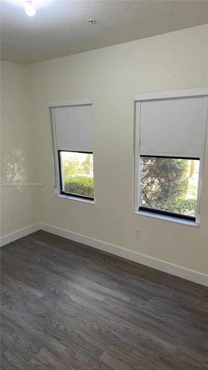 Room featuring wood-finish flooring, neutral wall paint, and two windows with white trim
