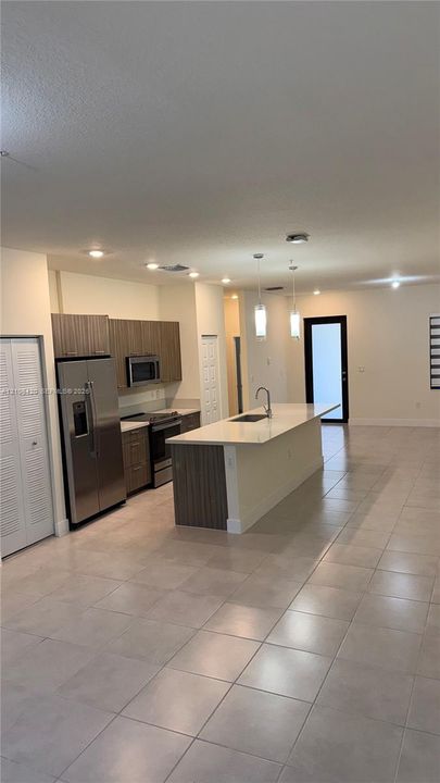 Kitchen featuring flat-panel cabinetry, a central island with a quartz countertop, stainless steel appliances, pendant lighting, and tile flooring