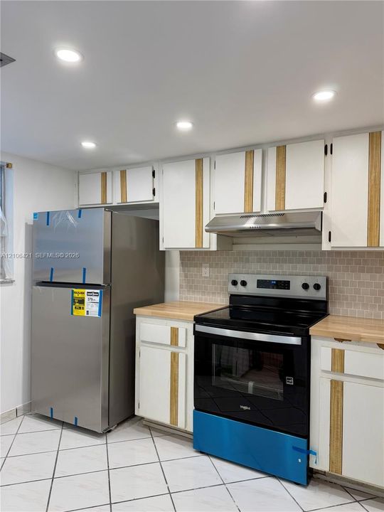 Kitchen featuring white cabinetry with wood-finish vertical accents, butcher-block countertops, a tiled backsplash, stainless steel appliances, and diagonal tile flooring