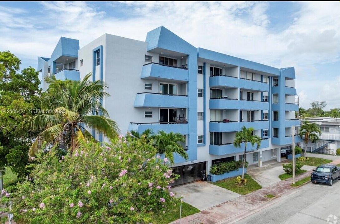 Mid-rise multi-unit residential building featuring a blue and white facade, private balconies, and gated ground-level parking