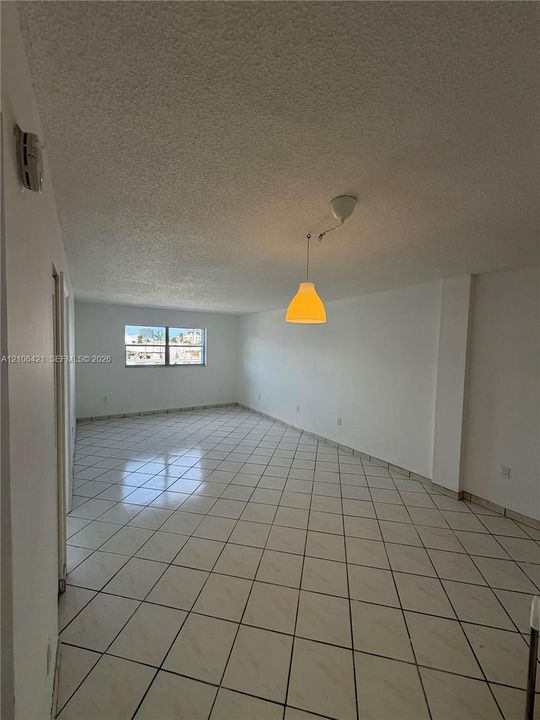 Open-concept interior featuring light-toned tile flooring, recessed ceiling finish, and a central pendant light fixture