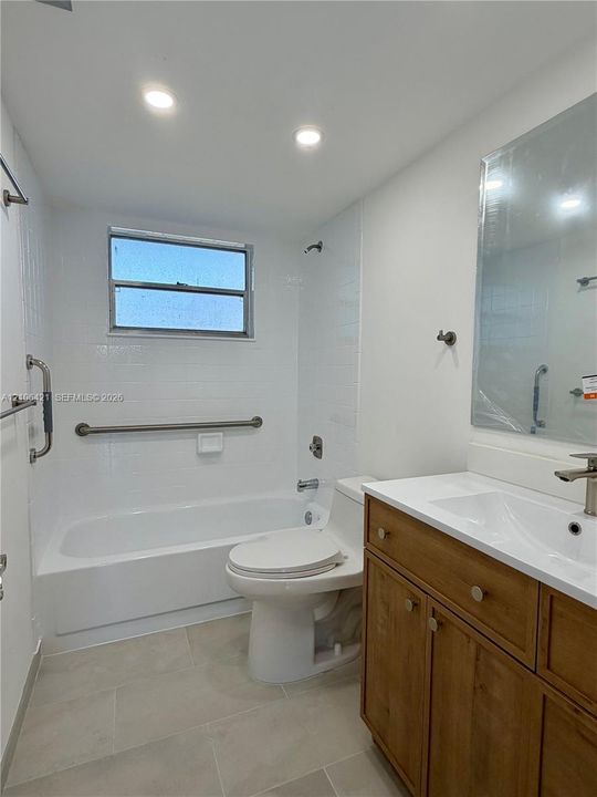 Bathroom featuring a vanity with a light wood finish, white countertop, integrated basin, recessed lighting, and white tile tub surround