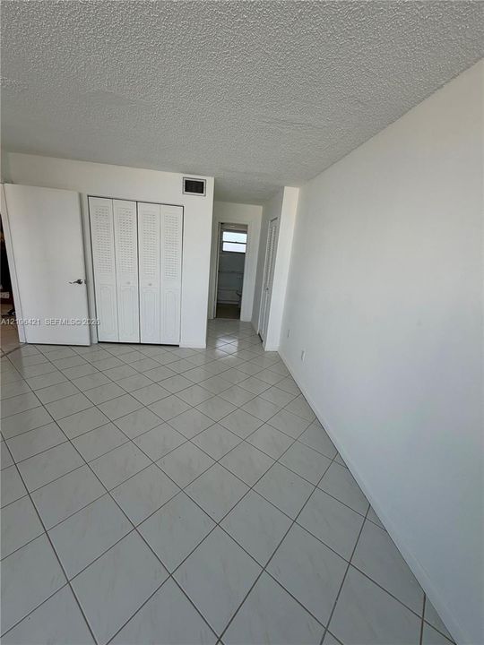 Neutral-toned tile flooring set in a diagonal pattern, white walls, and built-in closet storage with louvered doors