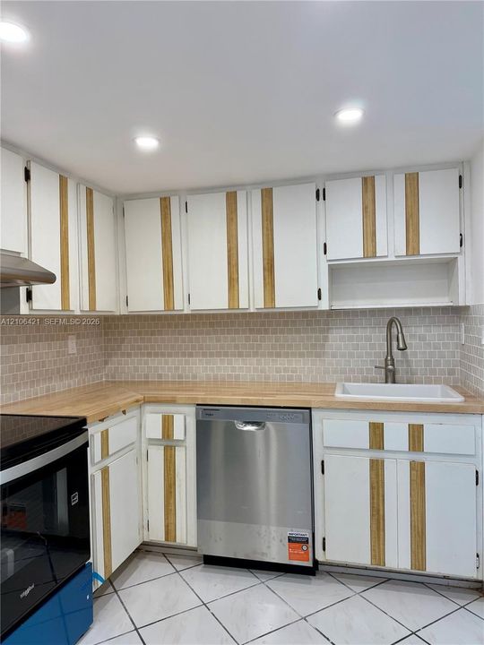 Kitchen featuring custom cabinetry with vertical wood accents, butcher block countertops, mosaic tile backsplash, stainless steel dishwasher, and recessed lighting