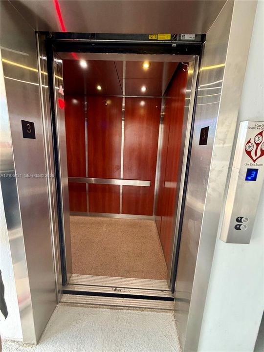 Elevator featuring wood-finish wall panels, stainless steel trim, recessed lighting, and a horizontal metal handrail