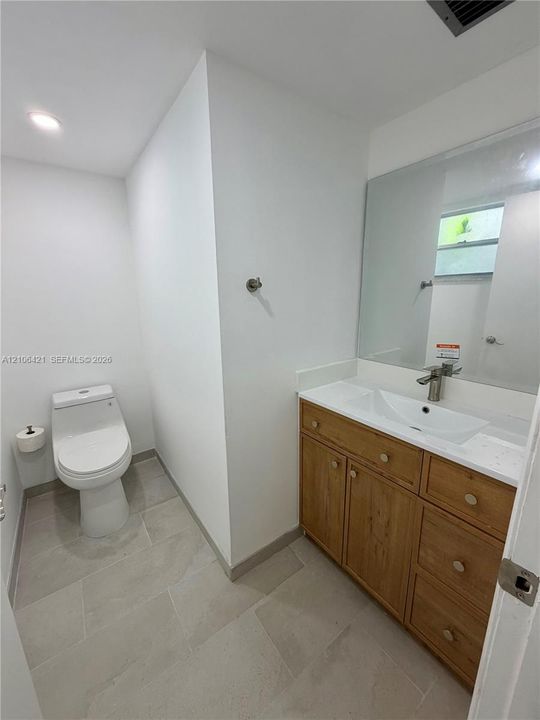 Bathroom featuring a wood-finish vanity with an integrated basin, large wall-mounted mirror, neutral tile flooring, and a modern dual-flush toilet