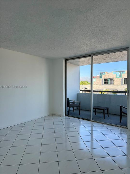 Interior space featuring white tile flooring and large sliding glass doors leading to a private balcony with a metal railing