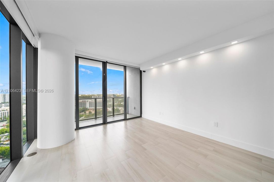 Floor-to-ceiling windows, wood-finish flooring, recessed ceiling lighting, and a private balcony featuring a metal railing