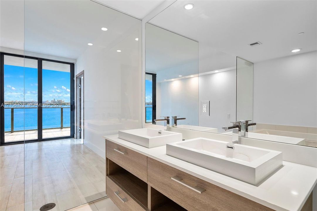 Dual vanity featuring rectangular vessel sinks, light wood-finish cabinetry, quartz countertops, and large wall-mounted mirrors