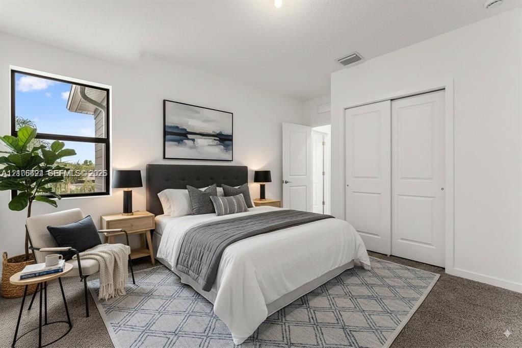 Neutral-toned room featuring wall-to-wall carpeting, dual-panel sliding closet doors, and a window with black trim