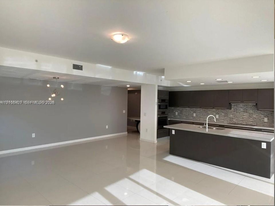 Kitchen featuring a central island with a solid-surface countertop, flat-panel cabinetry, a multi-textured stone tile backsplash, built-in double wall ovens, and large-format tile flooring