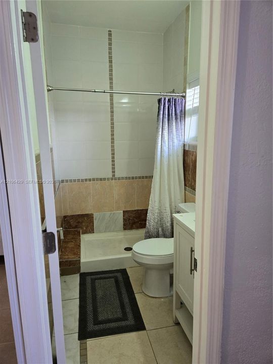 Bathroom featuring a standing shower with tiled surround, neutral-toned tile flooring, and a white vanity cabinet