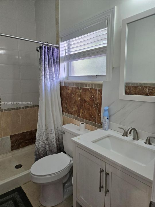 White vanity with integrated rectangular sink, stone-finish backsplash, neutral tile wall detailing, and a framed mirror
