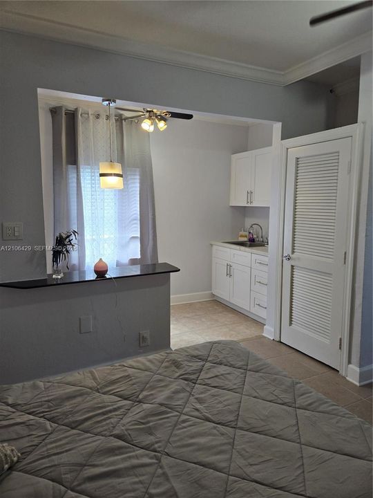 Kitchenette featuring white shaker-style cabinetry, solid-surface countertop with bar-style overhang, undermount sink, and louvered-panel door