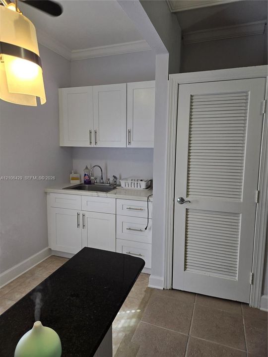 White shaker-style cabinetry with metallic pulls, stone-surface countertops, undermount stainless steel sink, and louvered door