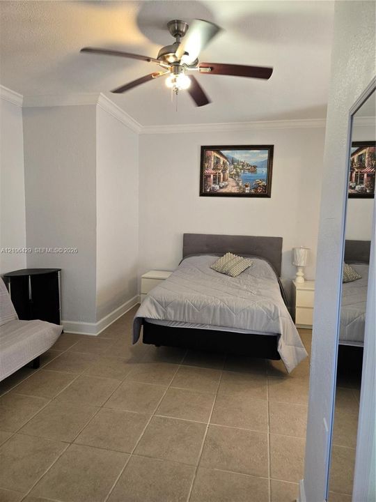 Room featuring neutral wall paint, tile flooring, crown molding, and a central ceiling fan with integrated light fixture