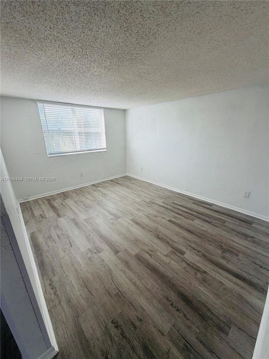 Neutral interior featuring wood-finish flooring, a textured ceiling, and a window with horizontal blinds
