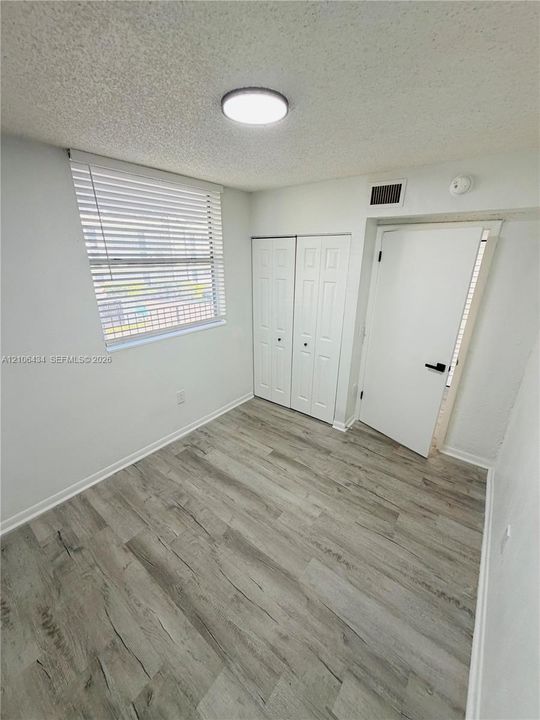 Room featuring wood-finish flooring, dual-panel closet doors, and horizontal window blinds
