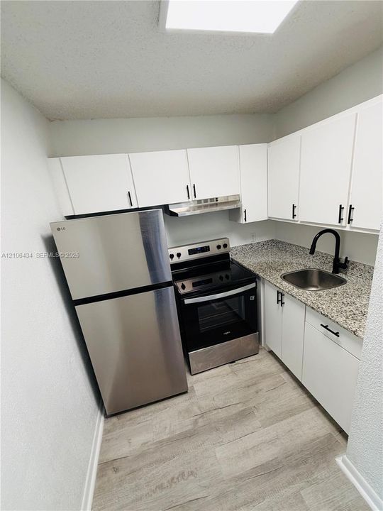Kitchen featuring white cabinetry with matte black hardware, stone-finish countertops, stainless steel appliances, and wood-finish flooring