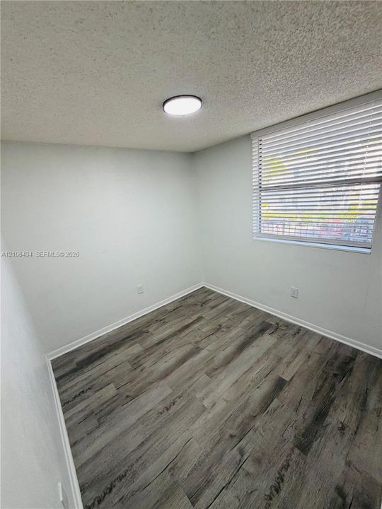Room featuring wood-finish flooring, neutral wall paint, and a window fitted with horizontal blinds