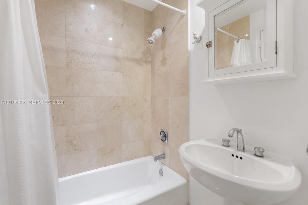 Full-height stone tile shower surround, pedestal sink with polished chrome fixtures, and white wall-mounted medicine cabinet