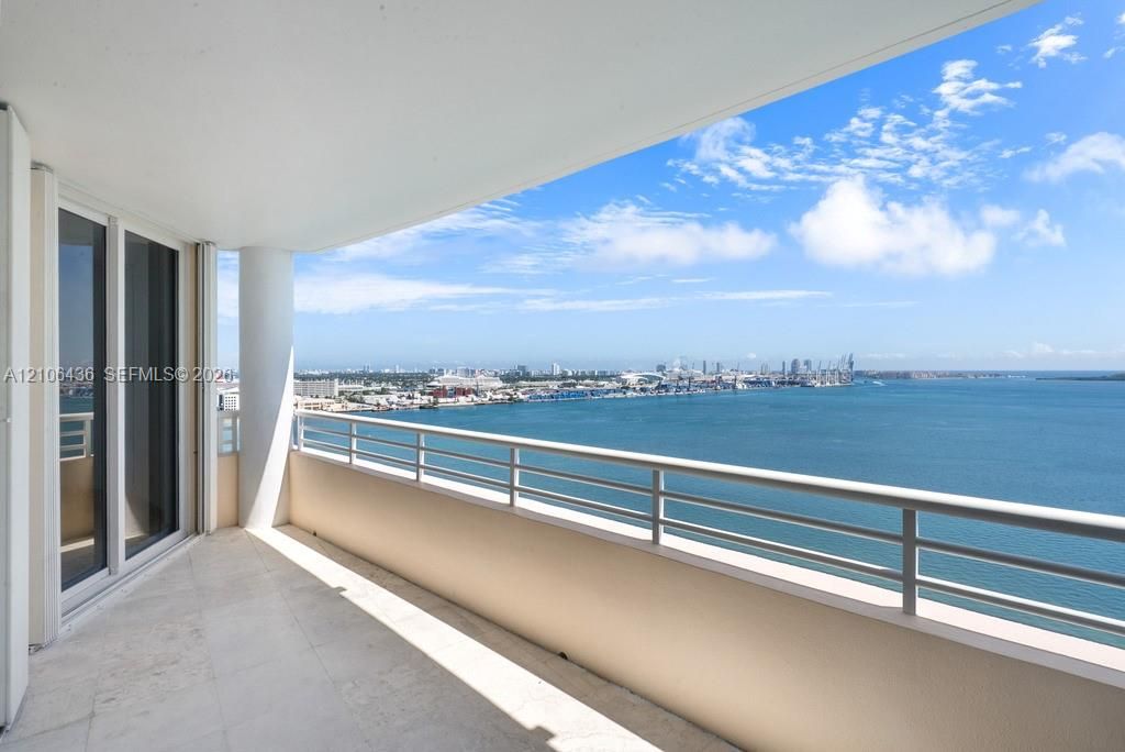 Covered balcony featuring stone-finish flooring, a sleek metal railing, a structural support column, and floor-to-ceiling glass sliding doors